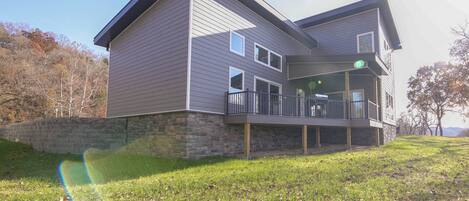 A two-story house with a stone foundation, a balcony, and a grassy yard.