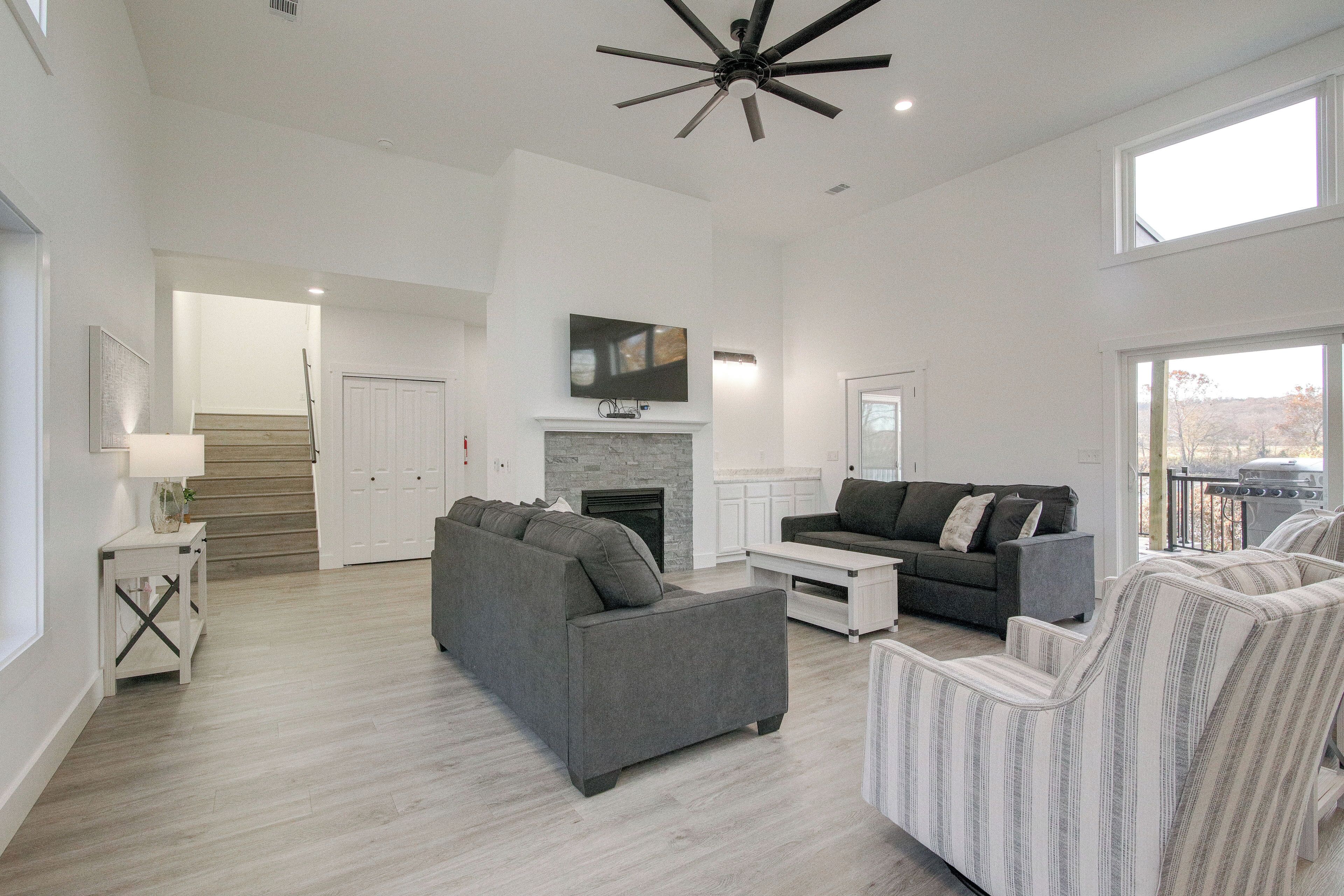 A spacious living room with a fireplace, grey sofas, and a ceiling fan.