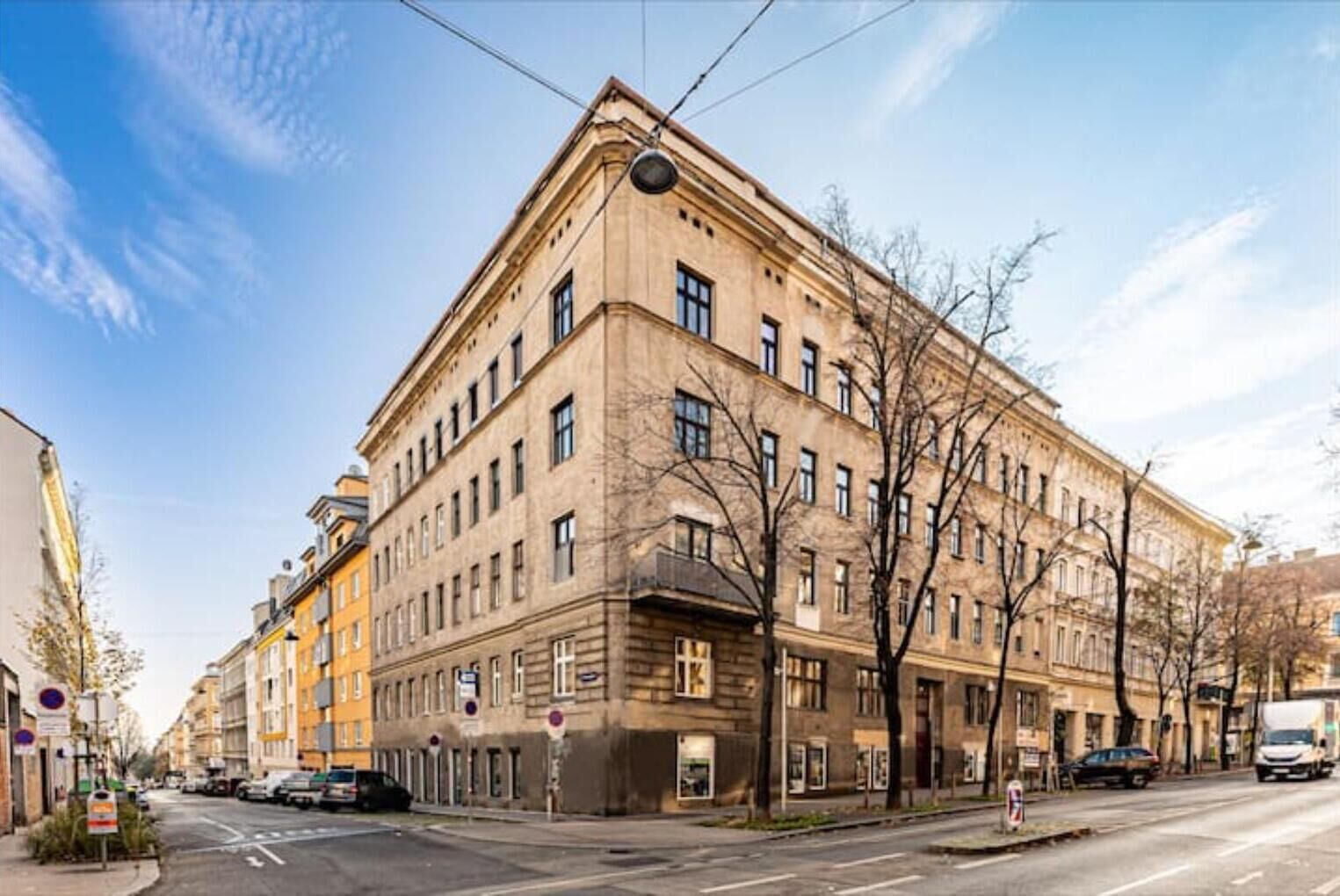 En stor, historisk byggnad med en entré i hörnet, många fönster och en slät fasad.