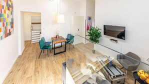 Una sala de estar moderna con piso de madera, una mesa de centro de vidrio, sillas color turquesa, un televisor montado en la pared y una planta en maceta.