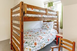 A bunk bed with floral bedding, a wooden chair, and a window with curtains.