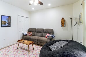A living room with a sofa, a coffee table, a bean bag, a ceiling fan, a framed picture, and a small boat decoration.