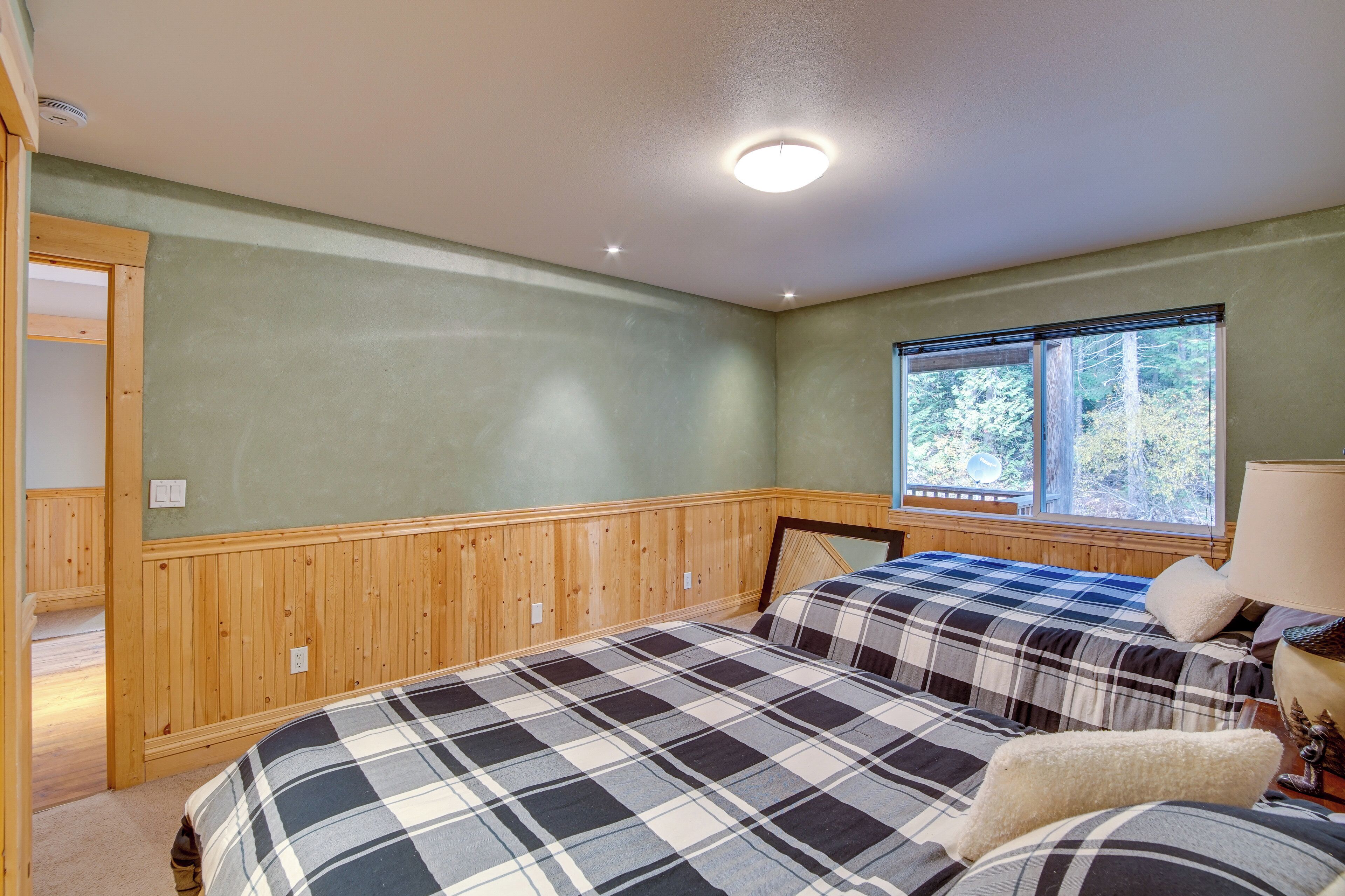 Une chambre avec deux lits, un lambris en bois, une fenêtre donnant sur des arbres et un luminaire au plafond.