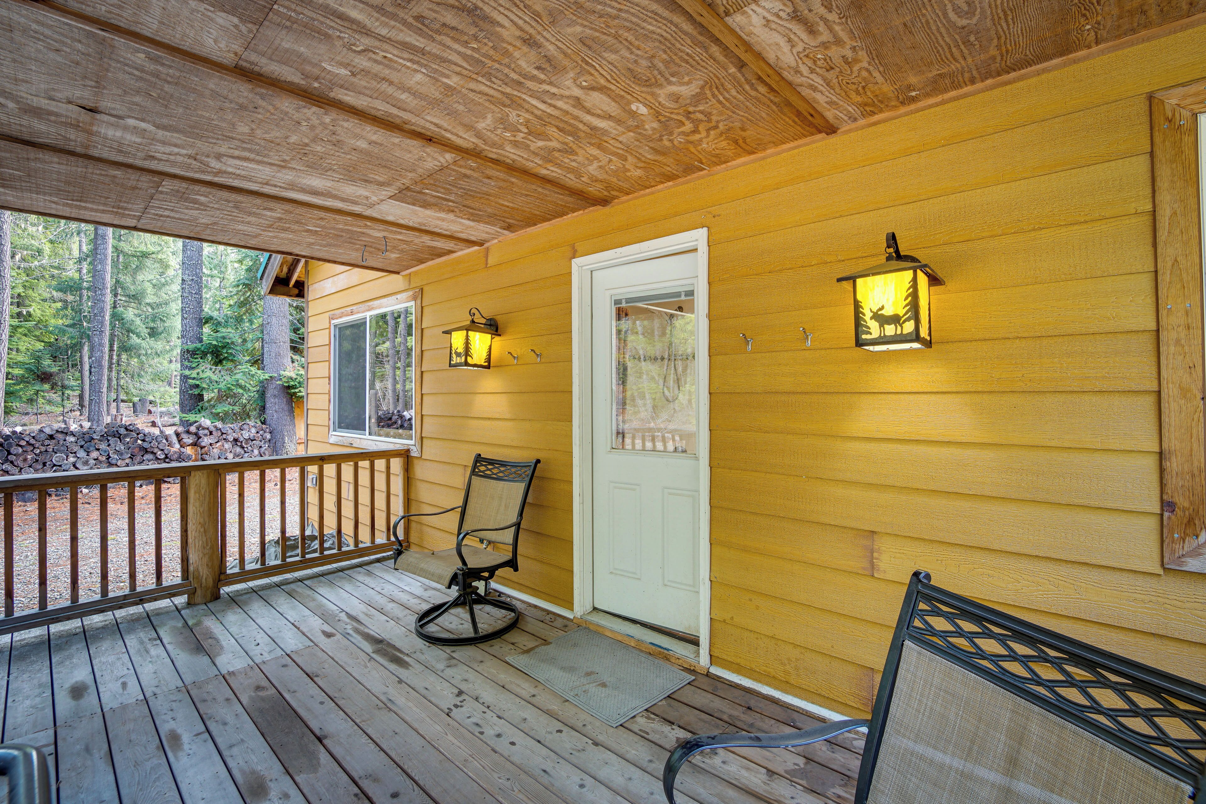 Une terrasse en bois avec deux chaises, une porte blanche et deux lanternes fixées au mur.
