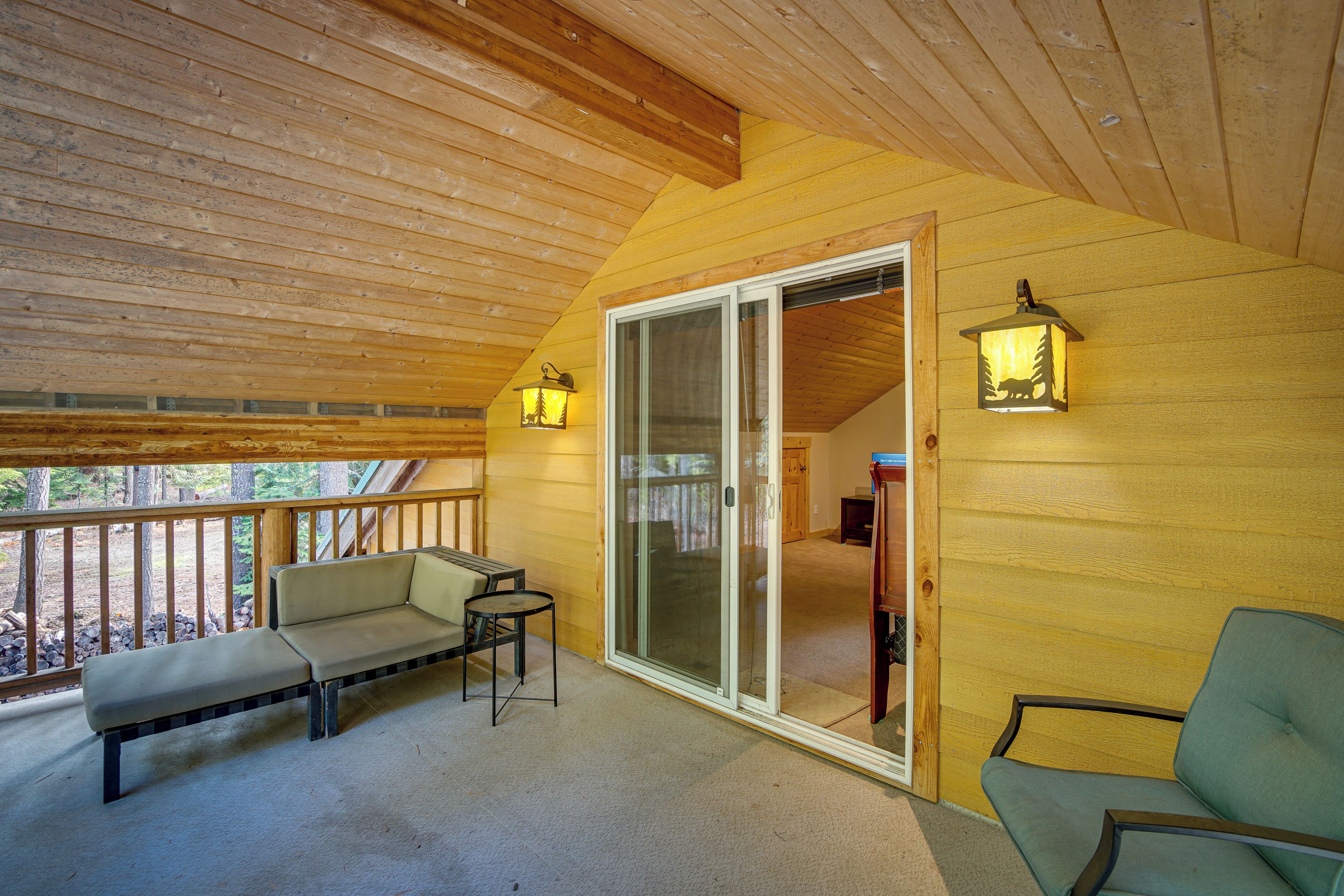 A wooden deck with a bench and a table, a sliding glass door, and two wall-mounted lanterns.