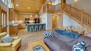 A spacious living area with a high ceiling, wooden staircase, and a cozy seating area. - 3 Mi to Lake Easton Sno-park: Family Cabin Escape! (Easton)