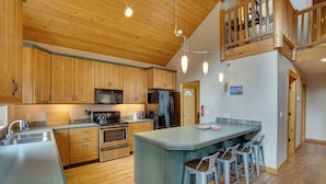 A kitchen with wooden cabinets, stainless steel appliances, and a bar area with stools. - 3 Mi to Lake Easton Sno-park: Family Cabin Escape! (Easton)