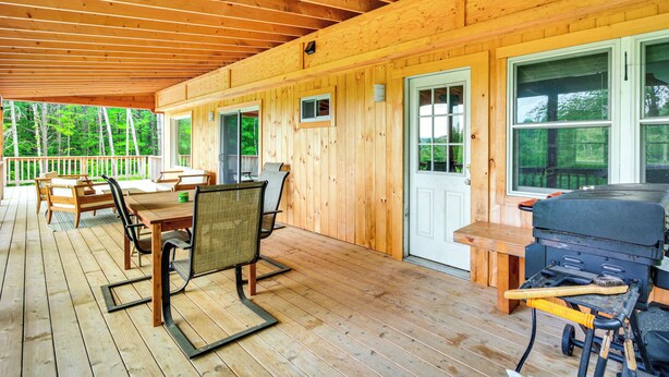 A wooden deck with a covered area, outdoor seating, and a barbecue grill.