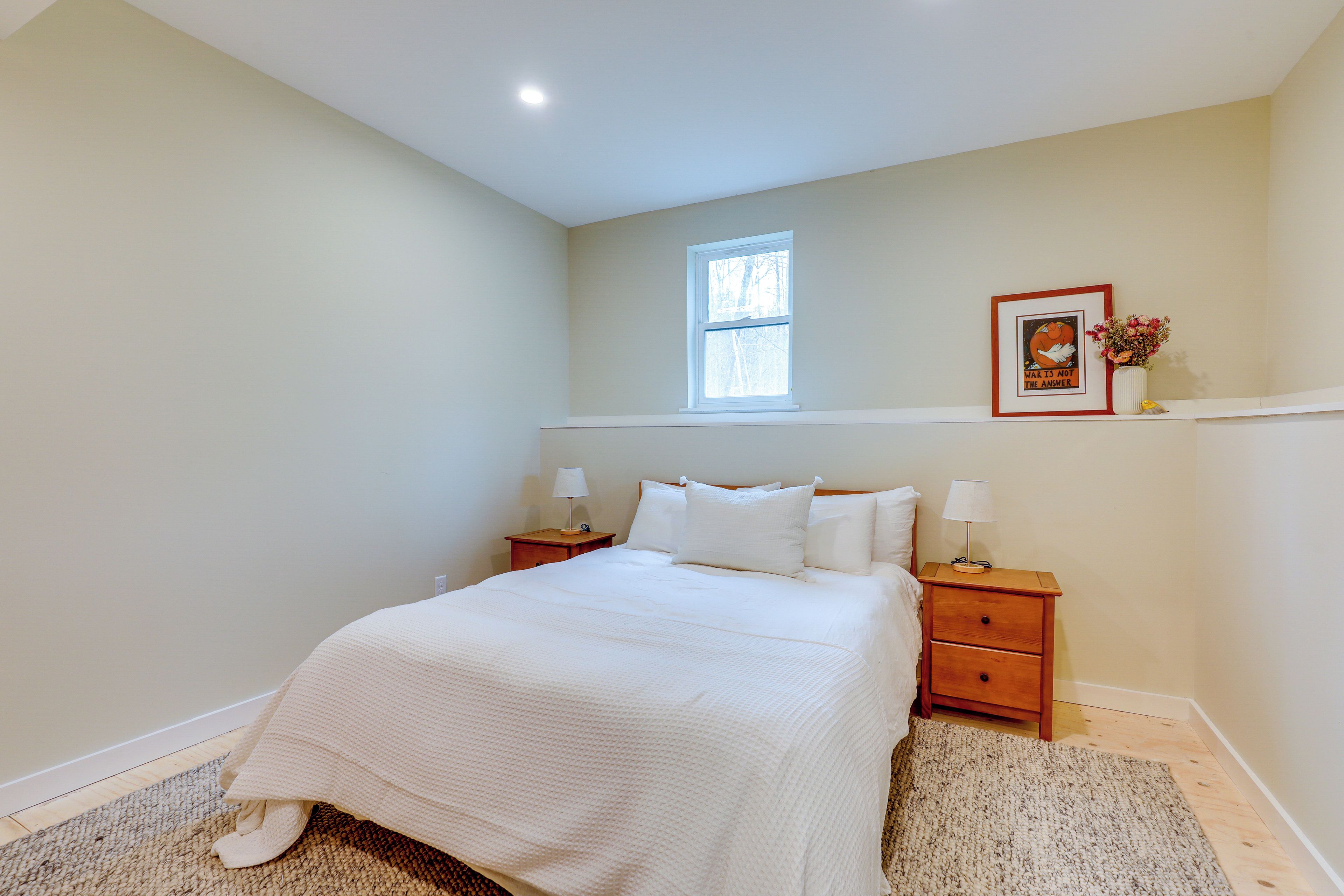 A bedroom with a large bed, two bedside tables, a window, and a framed picture on the wall.