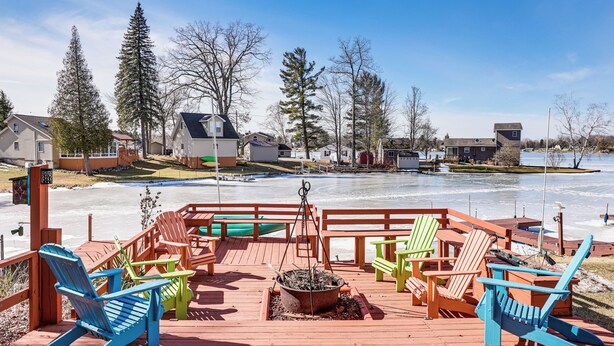 Puinen terassi, jossa on Adirondack-tyylisiä tuoleja ja nuotiopaikka, ja josta avautuu näkymä jäiselle järvelle, jonka taustalla näkyy taloja.
