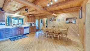 A wooden interior with a kitchen and dining area, featuring wooden cabinets, a dining table with chairs, and a ceiling with exposed beams and lights. - Secluded Log Cabin < 1 Mi to Munger State Trail! (Finlayson)