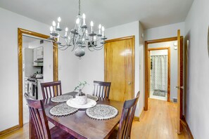 A dining room with a wooden table, six chairs, a chandelier, and a door leading to a kitchen.