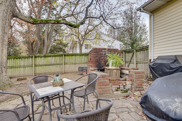 An outdoor patio with a brick grill, wicker chairs, and a table.
