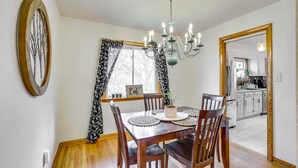 A dining area with a wooden table, chairs, a chandelier, and a window with patterned curtains. - Charming Arnold Home w/ Patio & Chicken Coop! (Arnold)