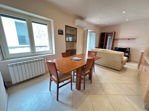 A dining area with a wooden table and chairs, a sofa, a TV, and a radiator.