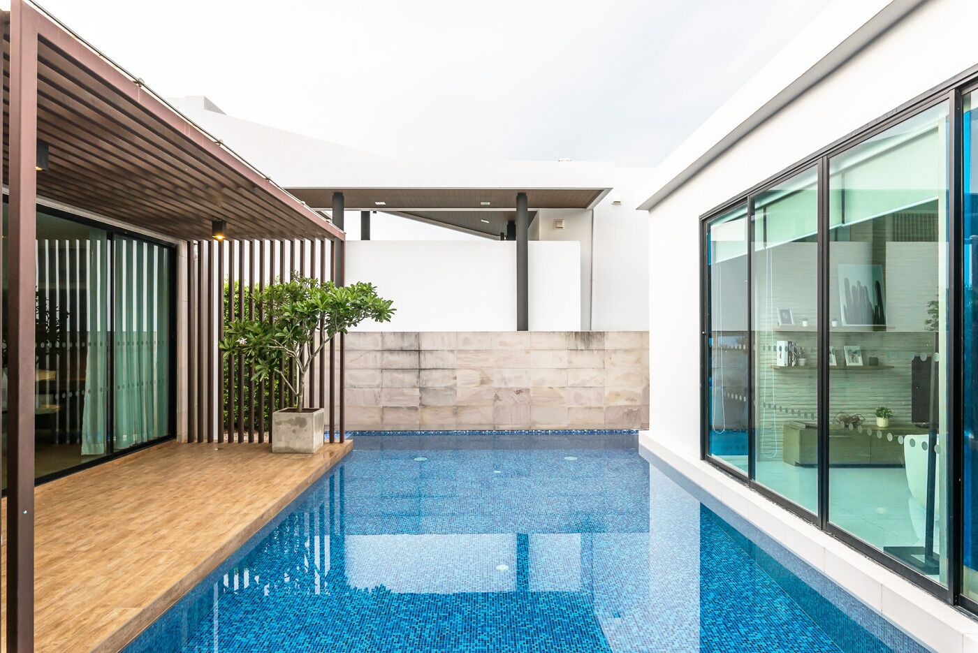 A modern indoor pool with a wooden deck and glass walls.