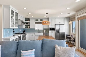 Une cuisine moderne avec des meubles blancs, un réfrigérateur en acier inoxydable et un coin repas comprenant une table et des chaises.