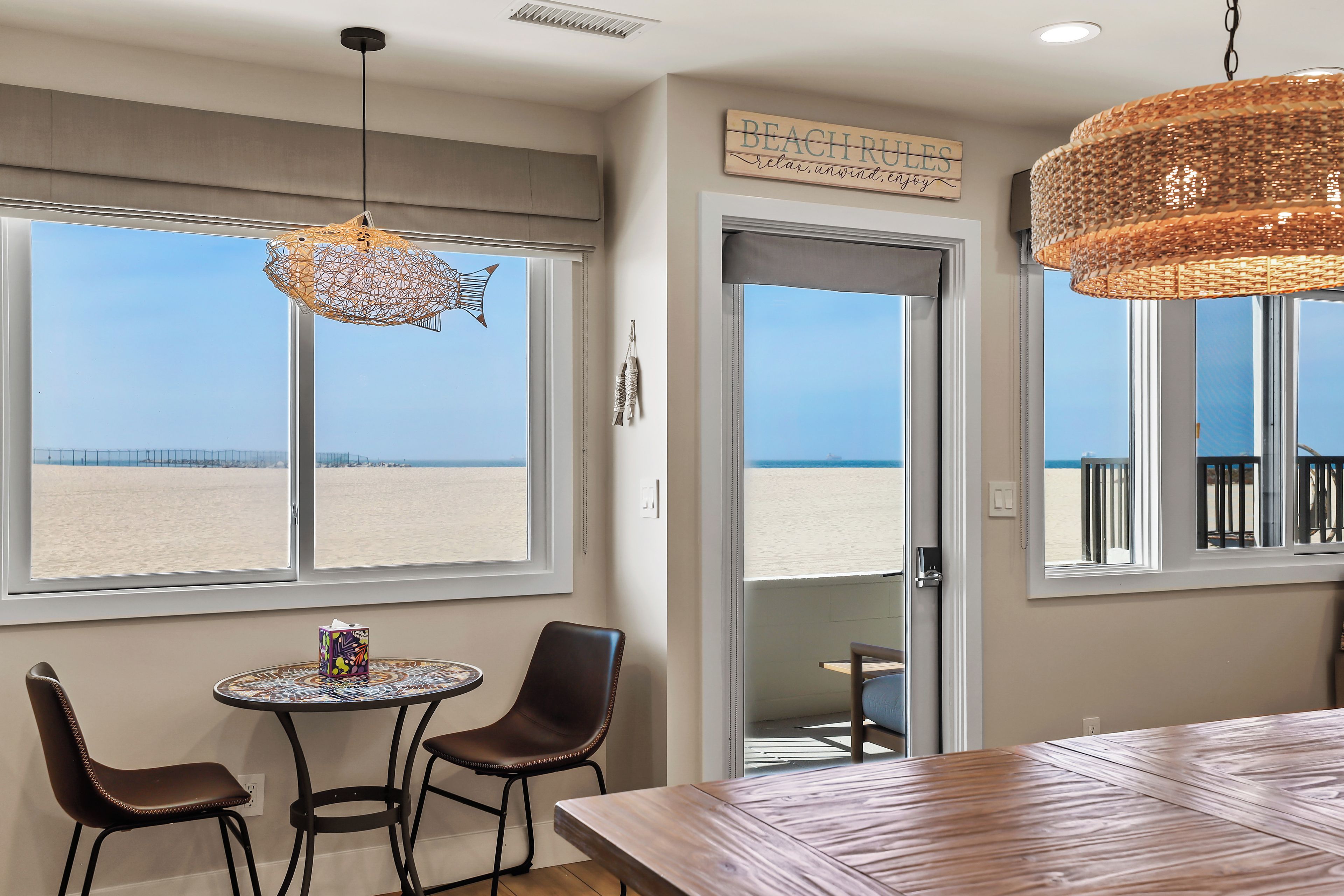 Una habitación con vista a la playa, un comedor con mesa y sillas, y una lámpara colgante.