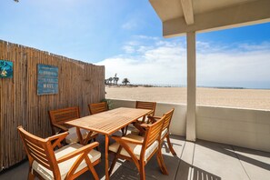 Un espace extérieur aménagé avec une table et des chaises en bois, une clôture en bambou et une vue sur la plage.