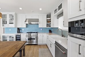 A modern kitchen with white cabinetry, a stainless steel stove, and a blue tiled backsplash. - ON THE SAND! Beachfront Seal Beach CA 3bd 3ba home (Seal Beach)