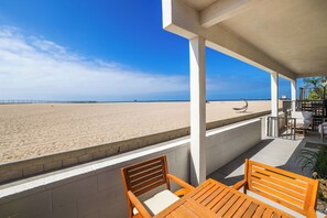 Une vue sur la plage depuis une terrasse couverte, aménagée avec des meubles en bois.
