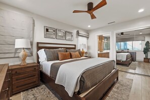 A bedroom with a large bed, bedside tables, a ceiling fan, and a view through a glass door.