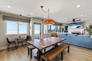 A modern interior with a dining area, a sofa, and a view of the sea.