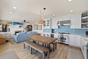 A modern kitchen with white cabinets, a built-in oven, and a dining area with a wooden table and bench. - ON THE SAND! Beachfront Seal Beach CA 3bd 3ba home (Seal Beach)