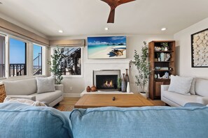 A living room with a fireplace, a large window, and a view of the beach.