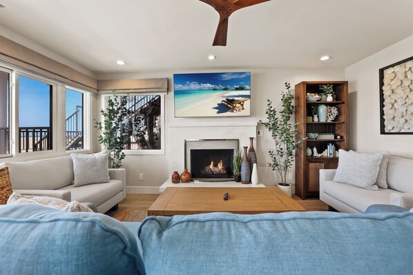 A living room with a fireplace, a large window, and a view of the beach.