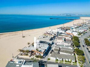 An aerial view of a coastal town with a beach, buildings, and a pier.
