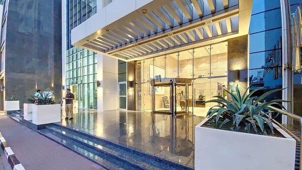 A modern hotel entrance with a glass facade, a covered outdoor area, and a reflective pool. - Neat 2 Bed l Media City Park l near Dubai Harbour (Dubai Marina)