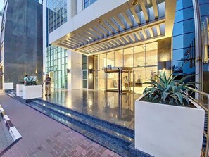 A modern hotel entrance with a glass facade, a covered outdoor area, and a reflective pool.