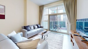 A modern living room with a sofa, coffee table, and a balcony with a table and chairs. - Neat 2 Bed l Media City Park l near Dubai Harbour (Dubai Marina)
