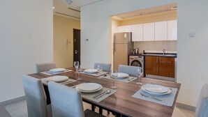 A dining area with a wooden table set for four, a kitchen with modern appliances, and a door leading to another room. - Neat 2 Bed l Media City Park l near Dubai Harbour (Dubai Marina)