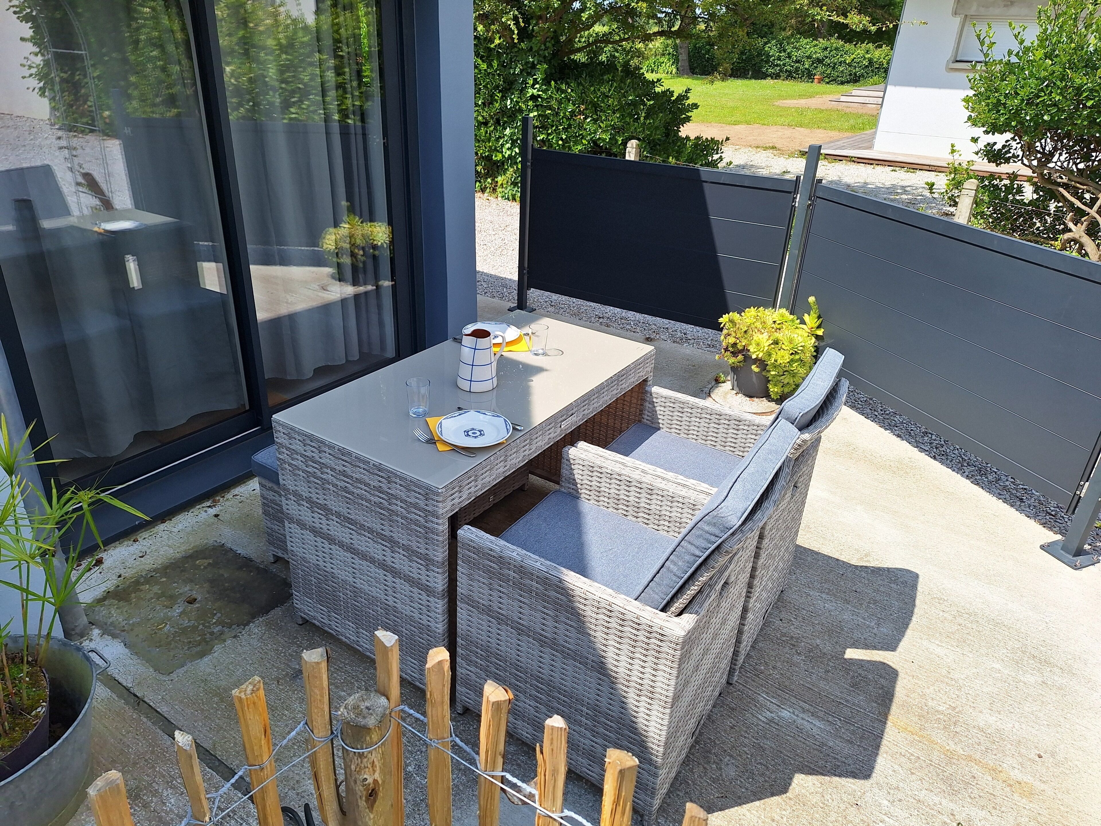 An outdoor patio with a table set for two, surrounded by wicker furniture and potted plants.