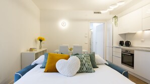 A modern hotel room with a bed, a bedside table with a vase of flowers, a small kitchen area, and a dining table with chairs. - notaMi - Little West (Milan)