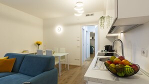 A modern kitchen with a fruit bowl on the counter, a dining area with a white table and chairs, and a blue sofa with a yellow pillow. - notaMi - Little West (Milan)
