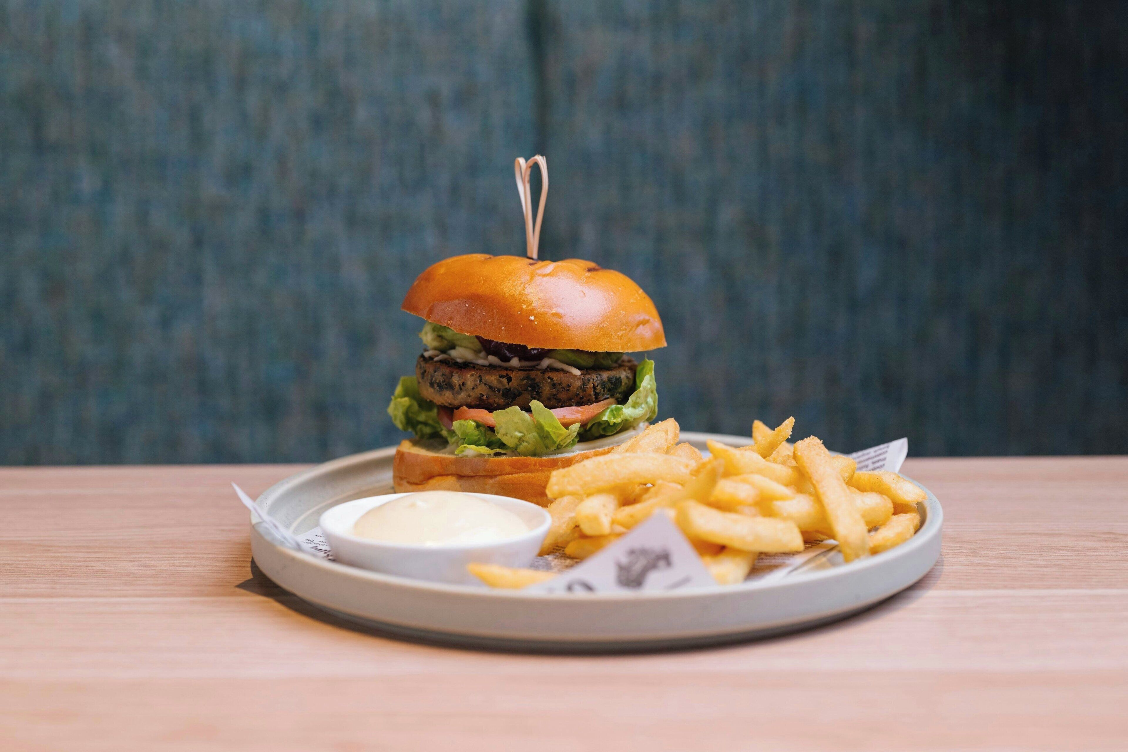 En hamburgare med en tandpetare på toppen, serverad med pommes frites och en liten skål med sås på en tallrik.
