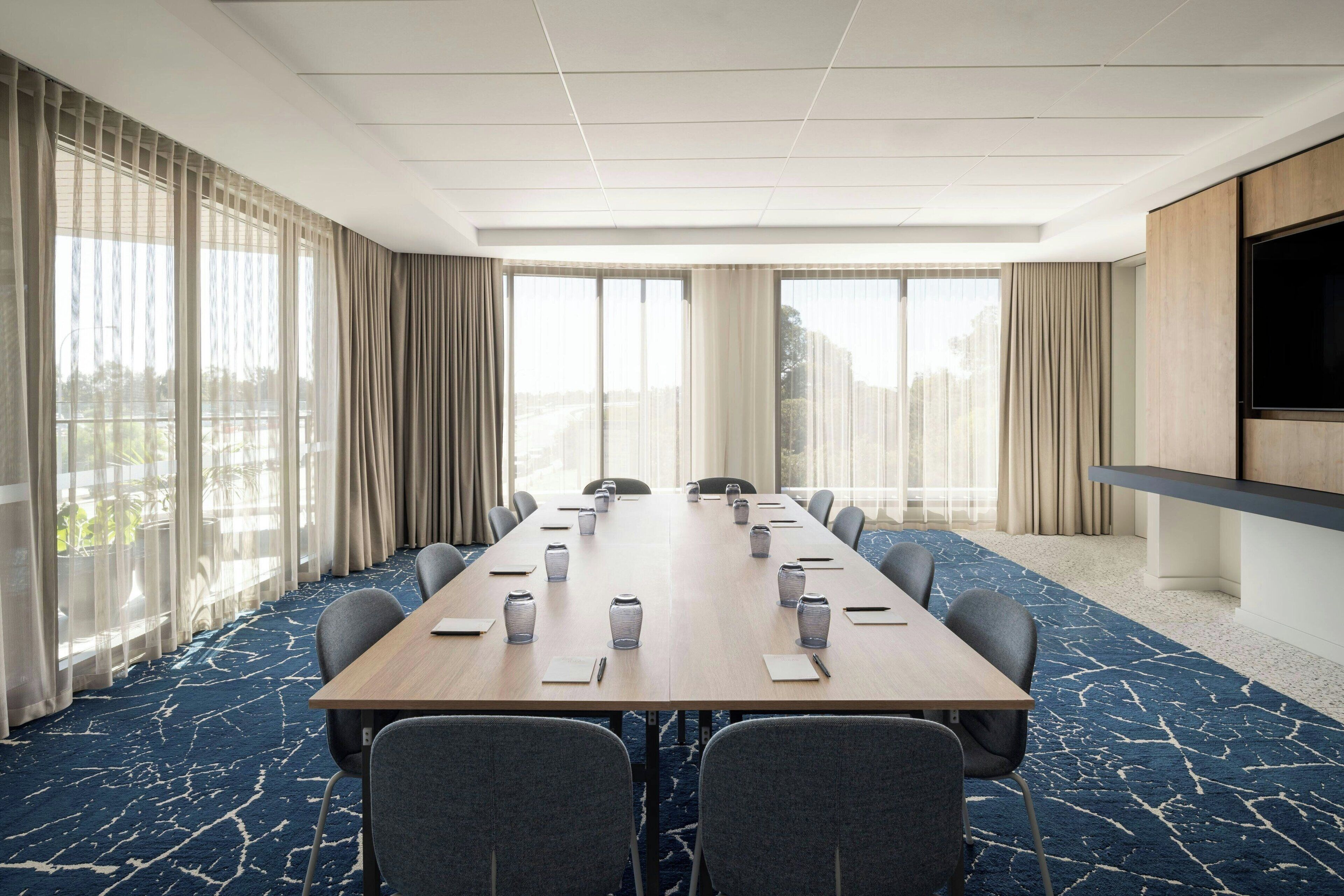 Un salón de conferencias con una larga mesa, sillas y un televisor en la pared.