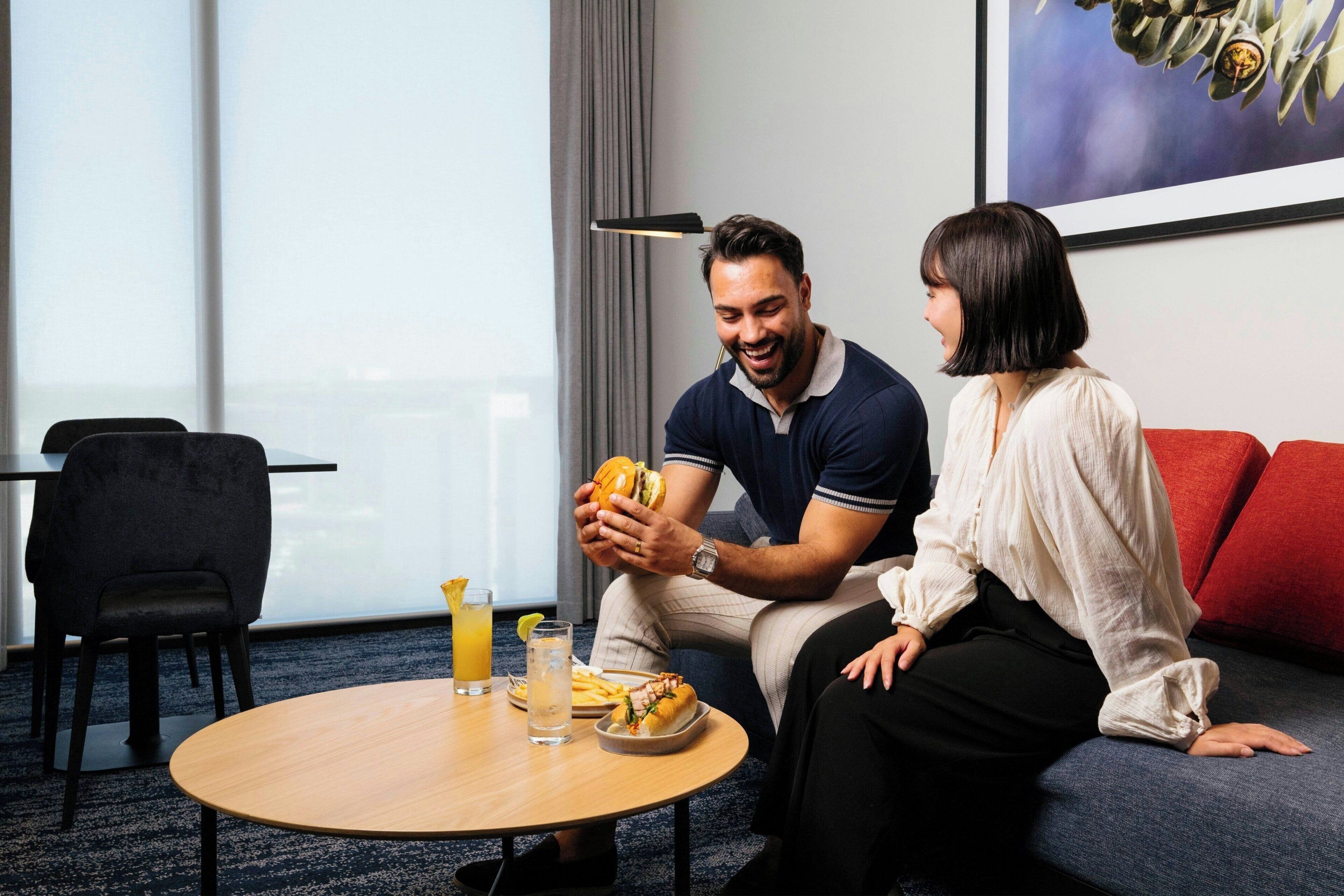 A room with a round wooden table, a sofa, and a chair. There is a plate with food and a drink on the table.