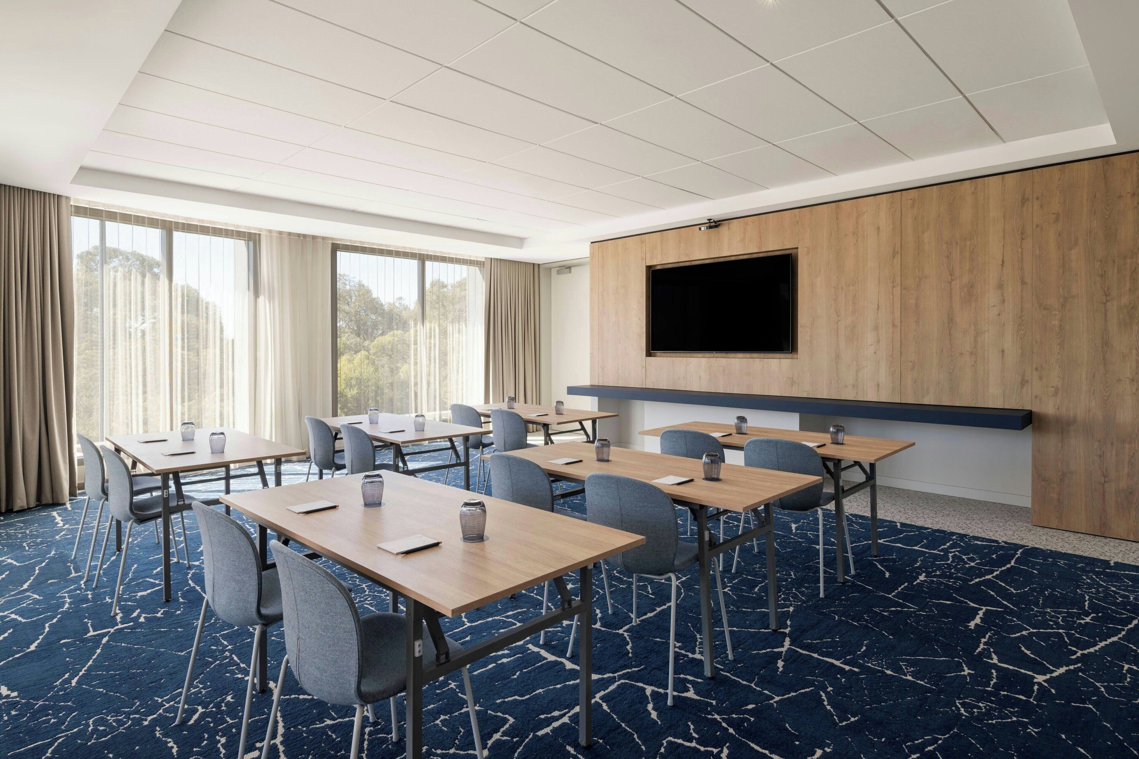 A conference room with multiple tables, chairs, a large screen, and a wooden panel wall.