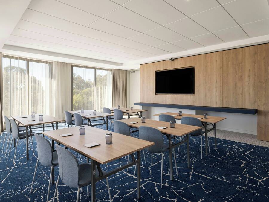Un salón de conferencias con varias mesas, sillas, una pantalla grande y un revestimiento de pared de madera.