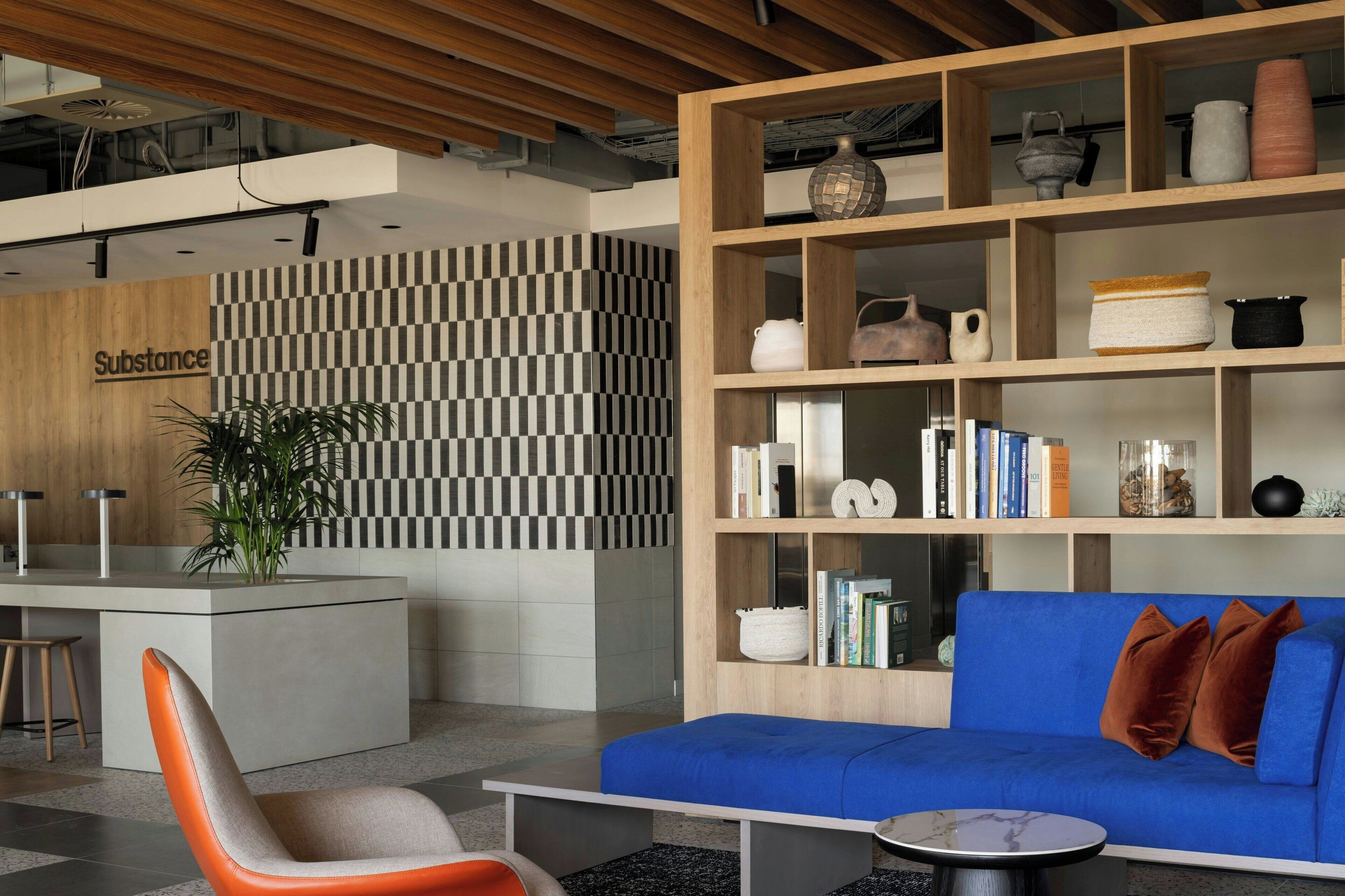A modern interior with a checkered wall, a blue sofa, a wooden bookshelf, and a reception desk labeled 'Substance'.