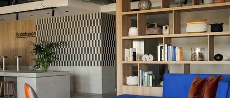 A modern interior with a checkered wall, a blue sofa, a wooden bookshelf, and a reception desk labeled 'Substance'.