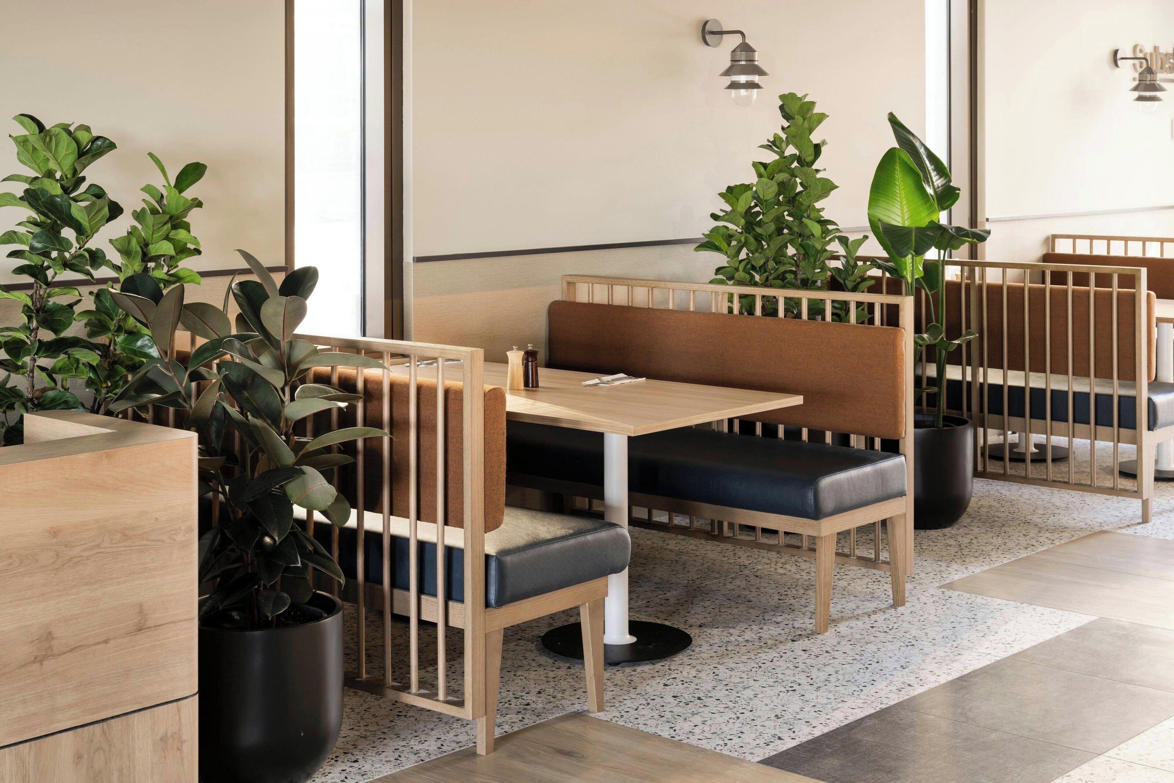 Un restaurante moderno con cabinas de madera, asientos acolchados negros y plantas en macetas.