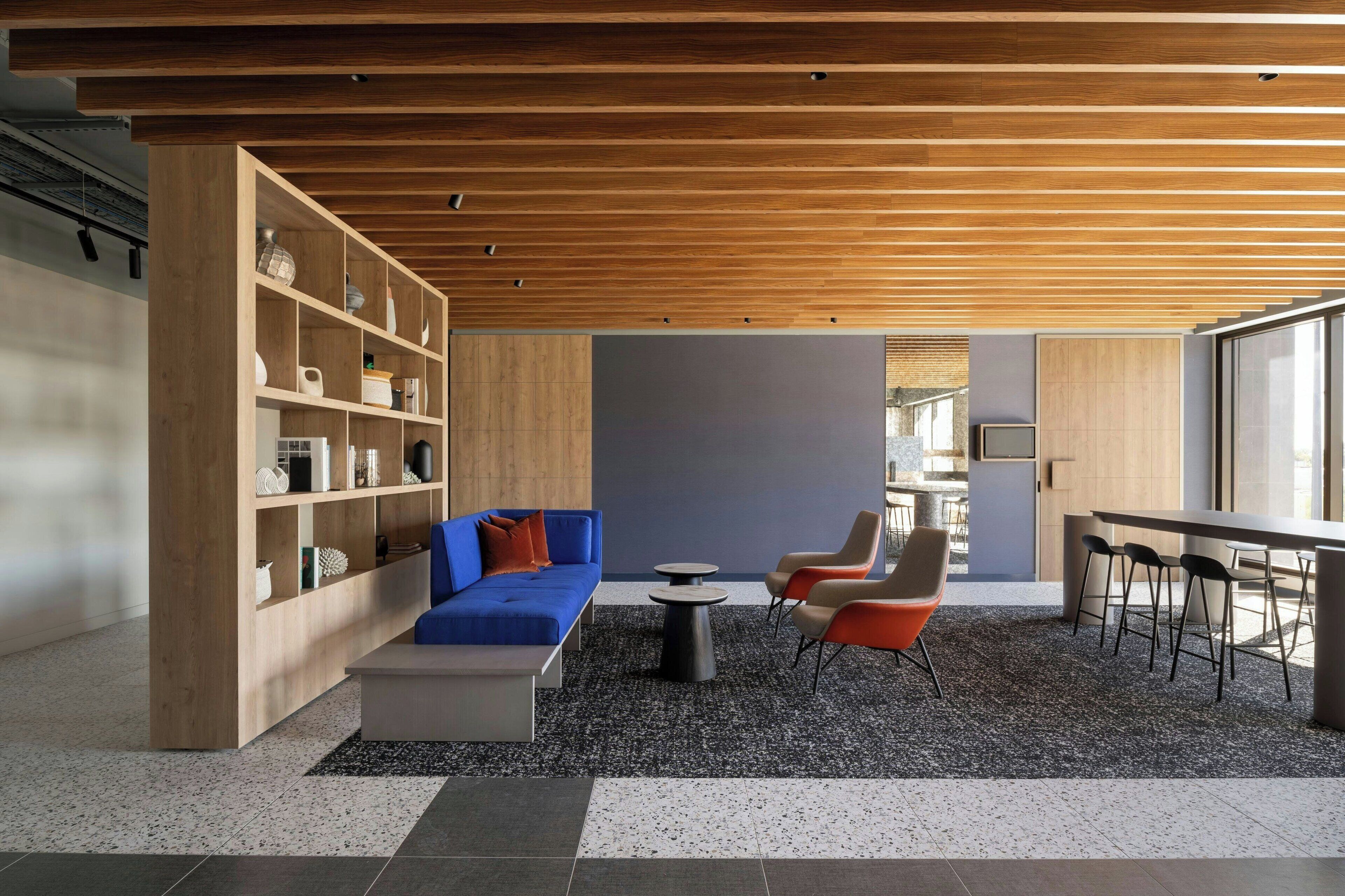 A modern interior with a wooden ceiling, a blue sofa, a coffee table, and a seating area with chairs.