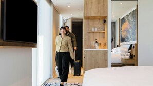 Habitación de hotel moderna con una cama grande, un televisor de pantalla plana en la pared, un mueble de madera con copas de vino y un cuadro en la pared.