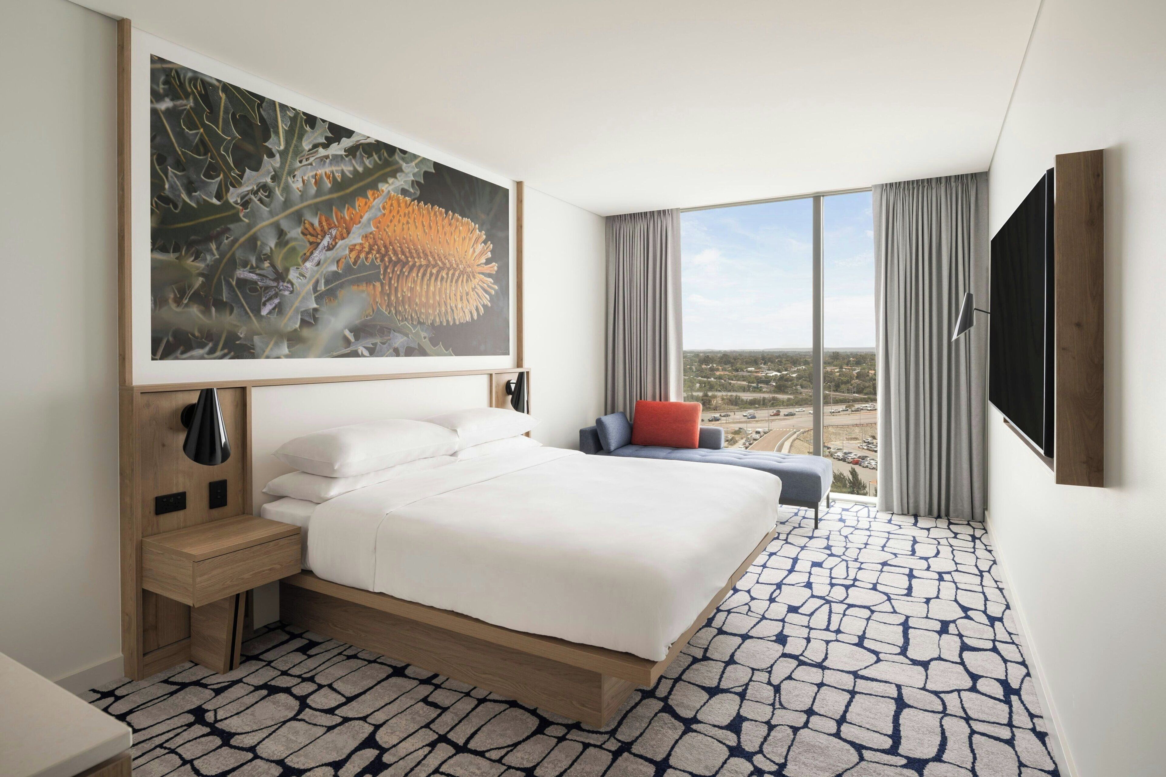Une chambre d’hôtel moderne dotée d’un grand lit, d’un bureau, d’une chaise et d’une grande fenêtre donnant sur la ville.