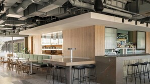 Un bar moderno con una barra alargada, taburetes y un área de estar con mesas y sillas.